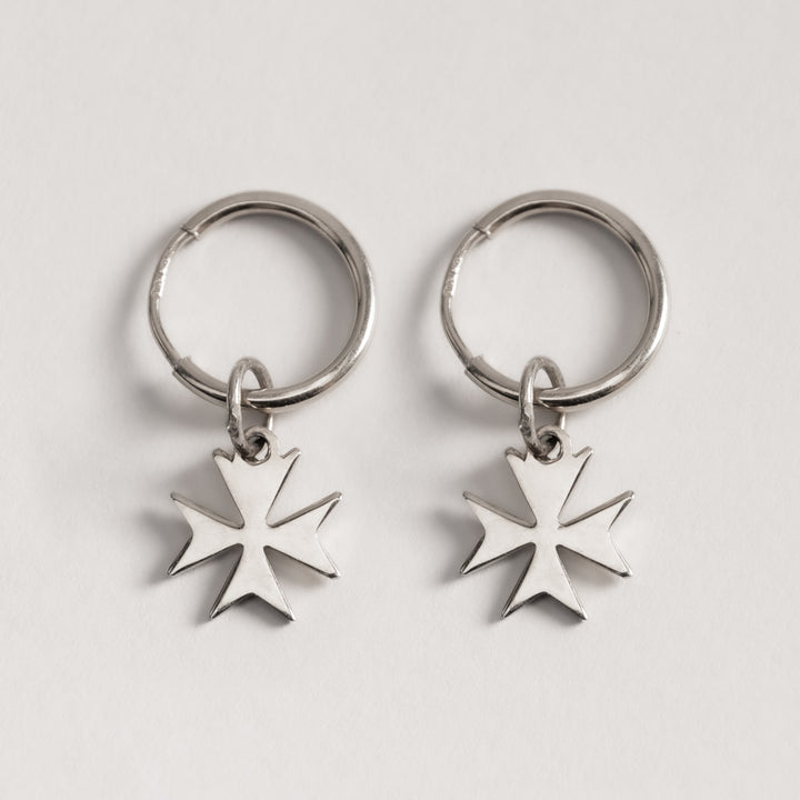 A close up view of Malta cross silver huggies standing in the center of the image against a white background. 