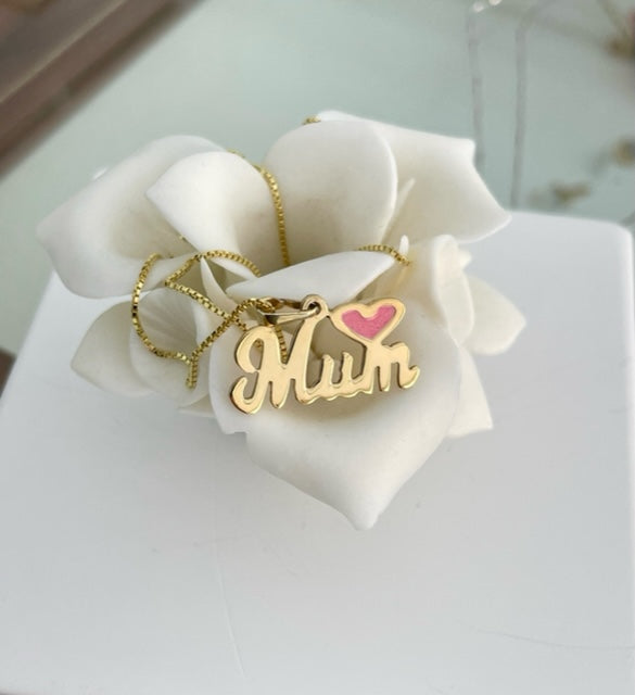 A yellow gold  Mum necklace with a heart-shaped pendant that reads 'MUM' on a white flower, presented on a white stand.