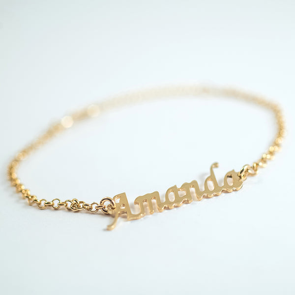 A gold-colored bracelet with the word 'Amanda' engraved on a chain of linked gold segments.