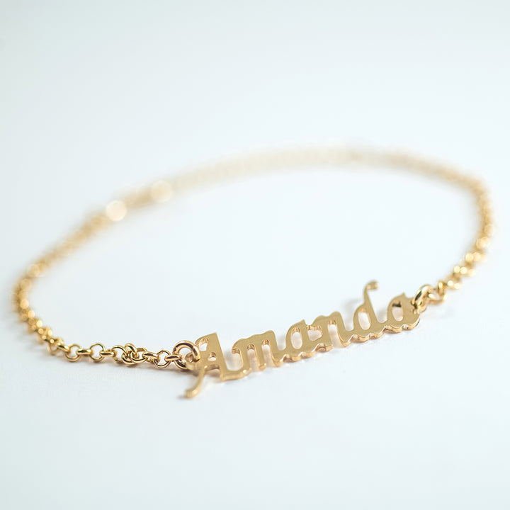 A gold-colored bracelet with the word 'Amanda' engraved on a chain of linked gold segments.