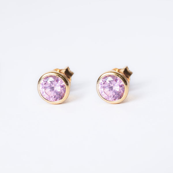 A pair of square-shaped stud October bird stone earrings with a yellow gold plated silver band and a pink gemstone in the center.