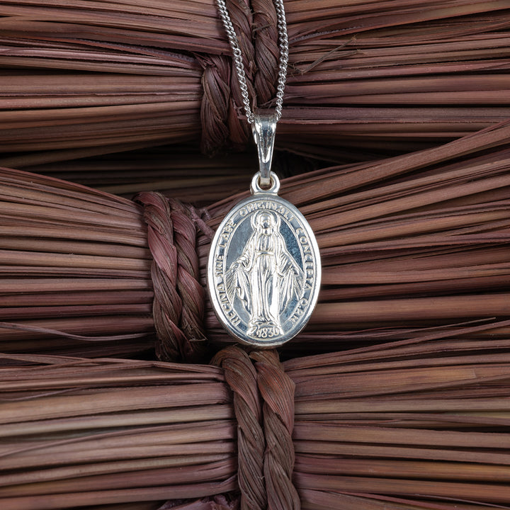 A close up view of Silver Holy Mary Charm Pendant against brown wooden sticks. 