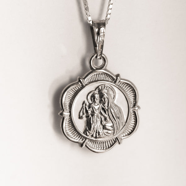 A silver double-sided pendant featuring an image of the Virgin Mary and baby Jesus.