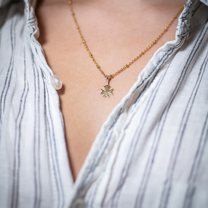 Woman wearing Melita Gold Maltese Cross Pendant on a naked skin, combined with her white shirt. 