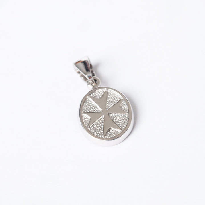 A silver Xandru pendant with a geometric star pattern in the center, attached to a small circular chain, seeing from a bird view angle. 